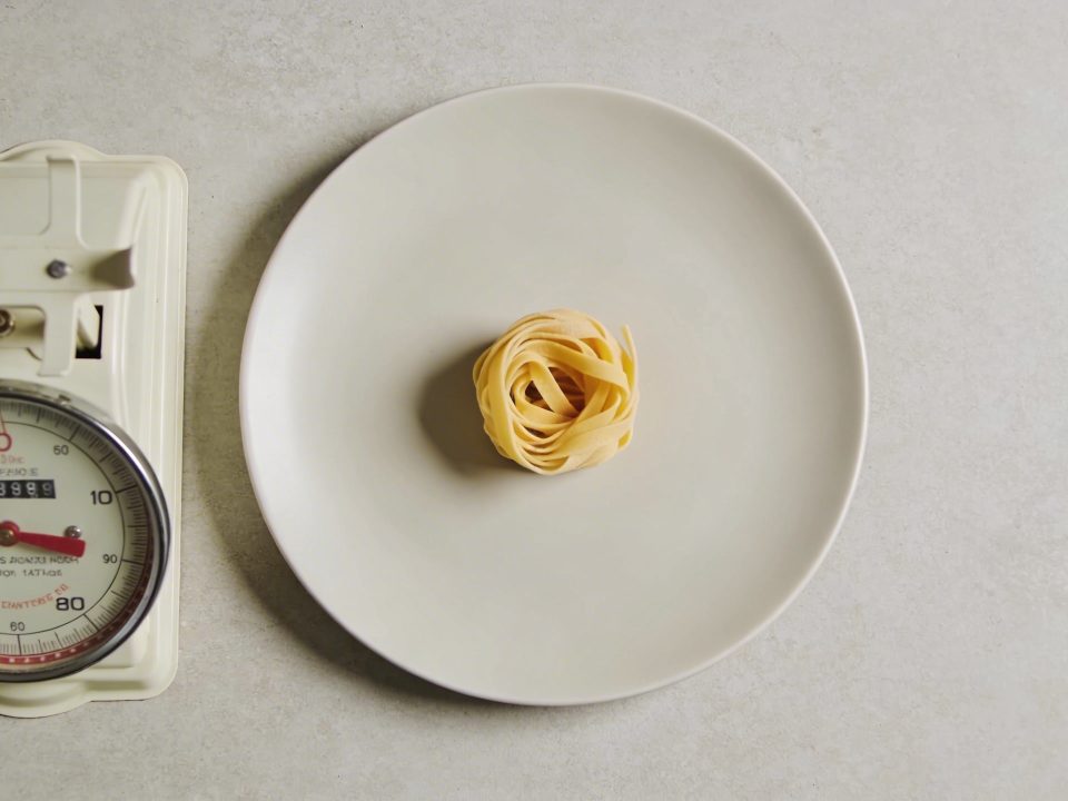 Assiette vue de dessus avec petite portion de pates et balance de cuisine