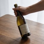 Main tenant une bouteille de vin 75 cl sur table