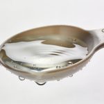 Petite cuillere doseuse remplie d eau sur fond blanc