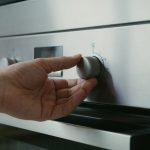 Main ouverte ajustant thermostat de four brillant