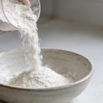 Main de cuisine versant farine blanche dans bol