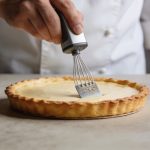 Main de cuisinier versant appareil sur fond de tarte