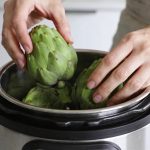 Mains plaçant des artichauts verts dans cocotte-minute