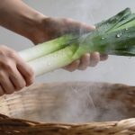 Mains disposant des poireaux sur panier vapeur fumant