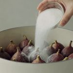 Mains versant sucre blanc dans grande casserole de figues