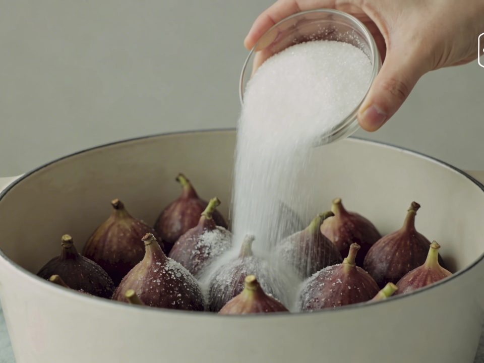 Mains versant sucre blanc dans grande casserole de figues