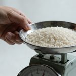 Main tenant une balance de cuisine pesant du riz