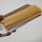 Main tenant une balance de cuisine avec spaghetti crus