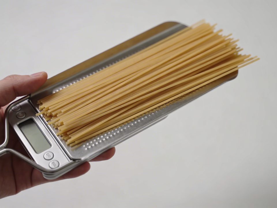 Main tenant une balance de cuisine avec spaghetti crus