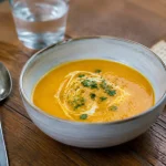 Bol de veloute orange servi sur table en bois