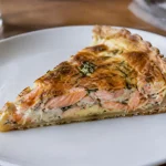 Part de tarte au saumon posee sur assiette blanche