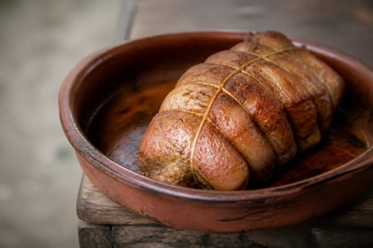 Viande dorée ficelée posée sur plat en terre cuite
